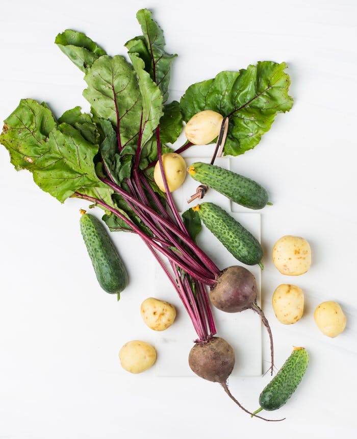 Assorted organic vegetables including beets, cucumbers, and potatoes on a white surface.