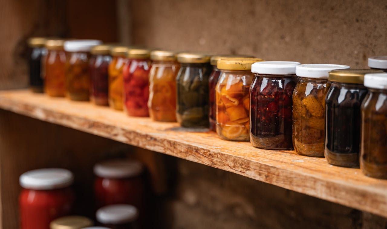 Homemade preserves in mason jars neatly arranged on a rustic wooden shelf.